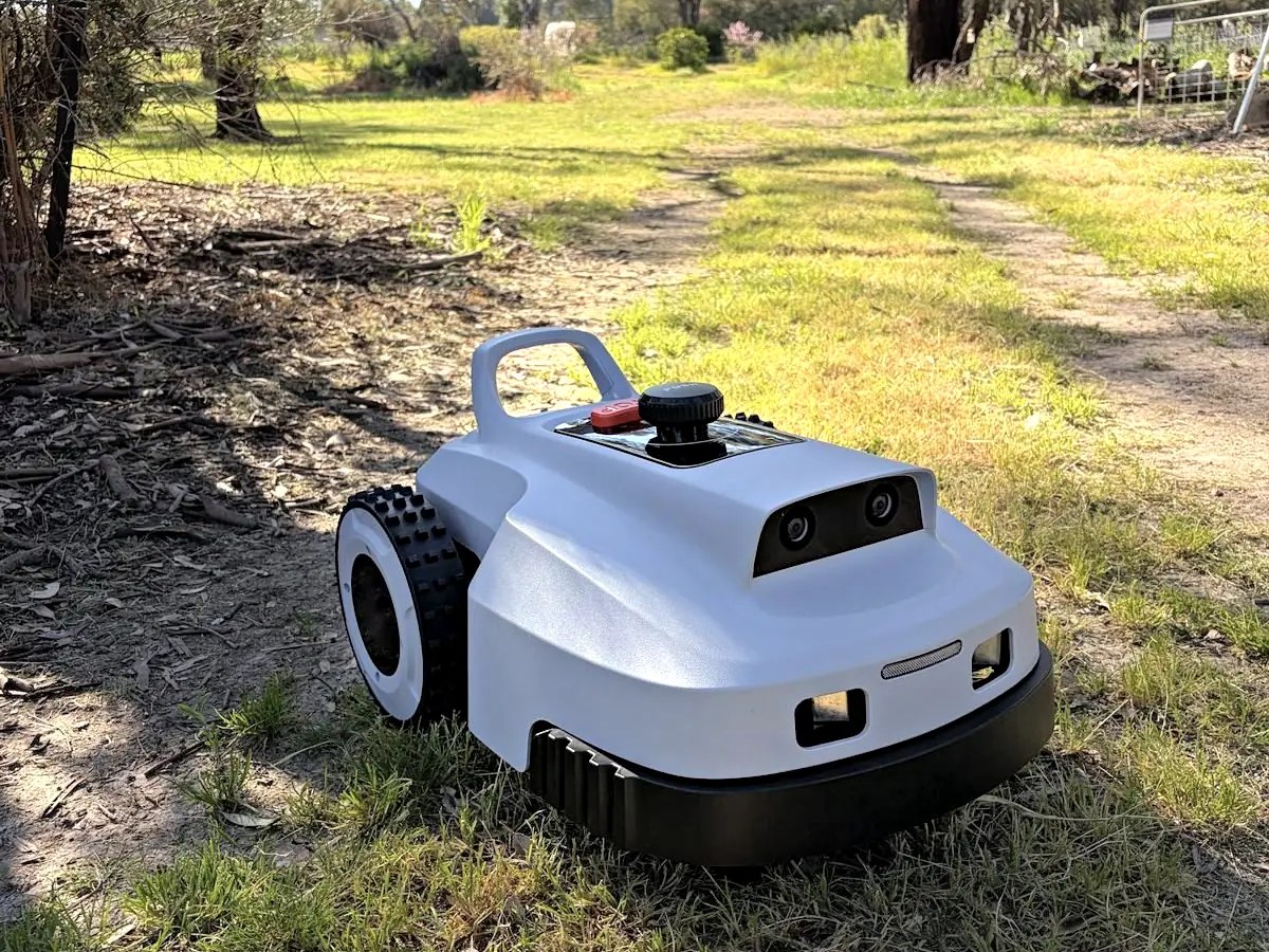 Mini Kelpie robotic mower on a grass track under gum trees.